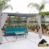 A covered patio with teal outdoor seating, a coffee table, and white curtains. Palm trees and plants surround the area. "Dog Park Outfitters" logo with a black dog is in the bottom right corner.