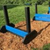 A Jump Hurdle - Small is set up on mulch in a grassy outdoor dog park, likely within a fenced area with green trees in the background.