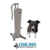 A black and white dog sits by a tall, silver and beige Doggie Demand COOL DOG Portable Fresh Flow Water Fountain – Hooks up to Garden Hose (SLV). Below them is the "COOL DOG WATER FOUNTAINS.COM" logo with a dog silhouette.