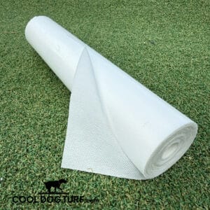 A roll of white geotextile fabric is partially unrolled on artificial grass. The fabric has a textured surface, and the green turf beneath creates a contrasting background. The logo "COOLDOGTURF.com" is visible in the corner.